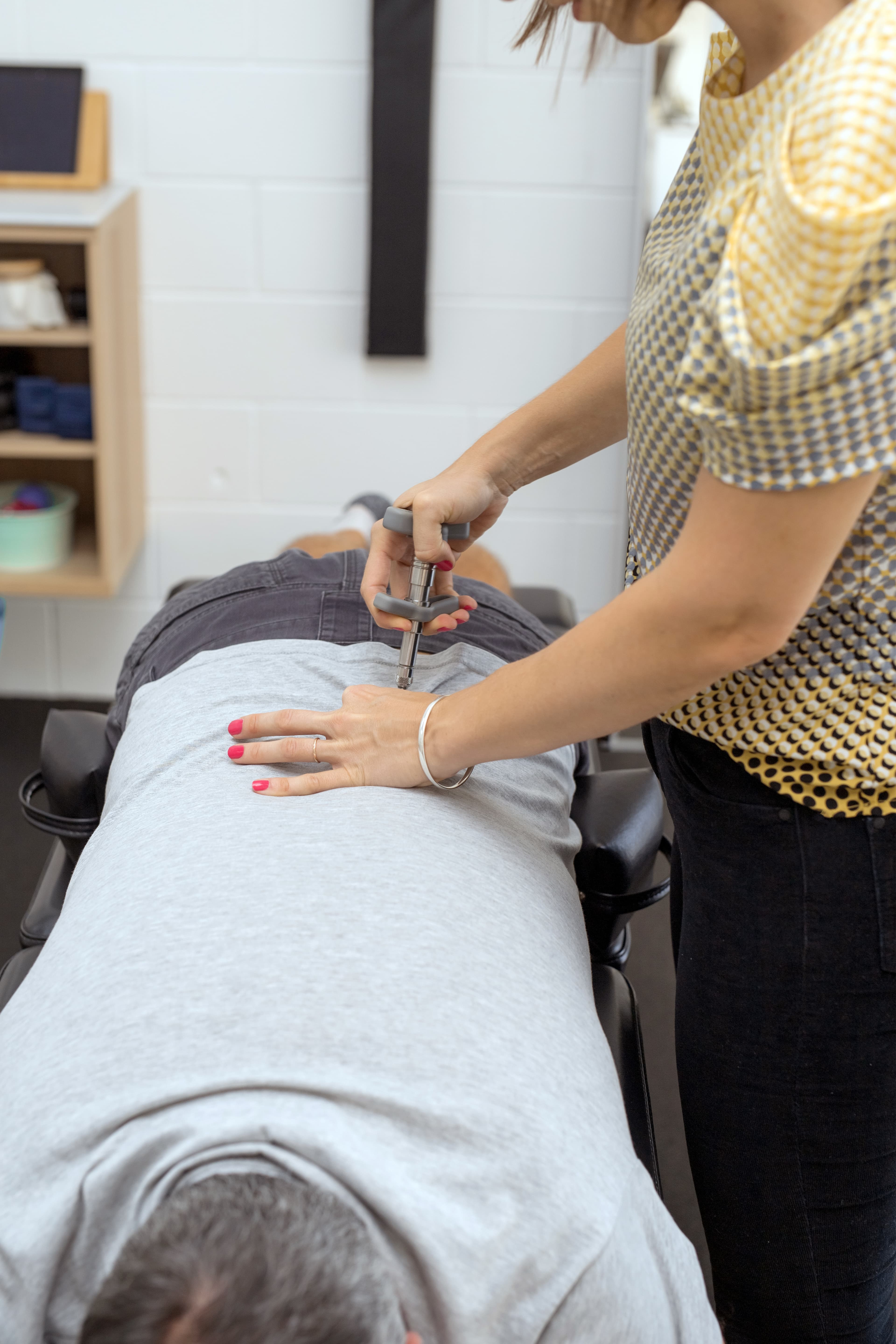 Chiropractor performing a spinal adjustment on a patient's back using a handheld activator tool.