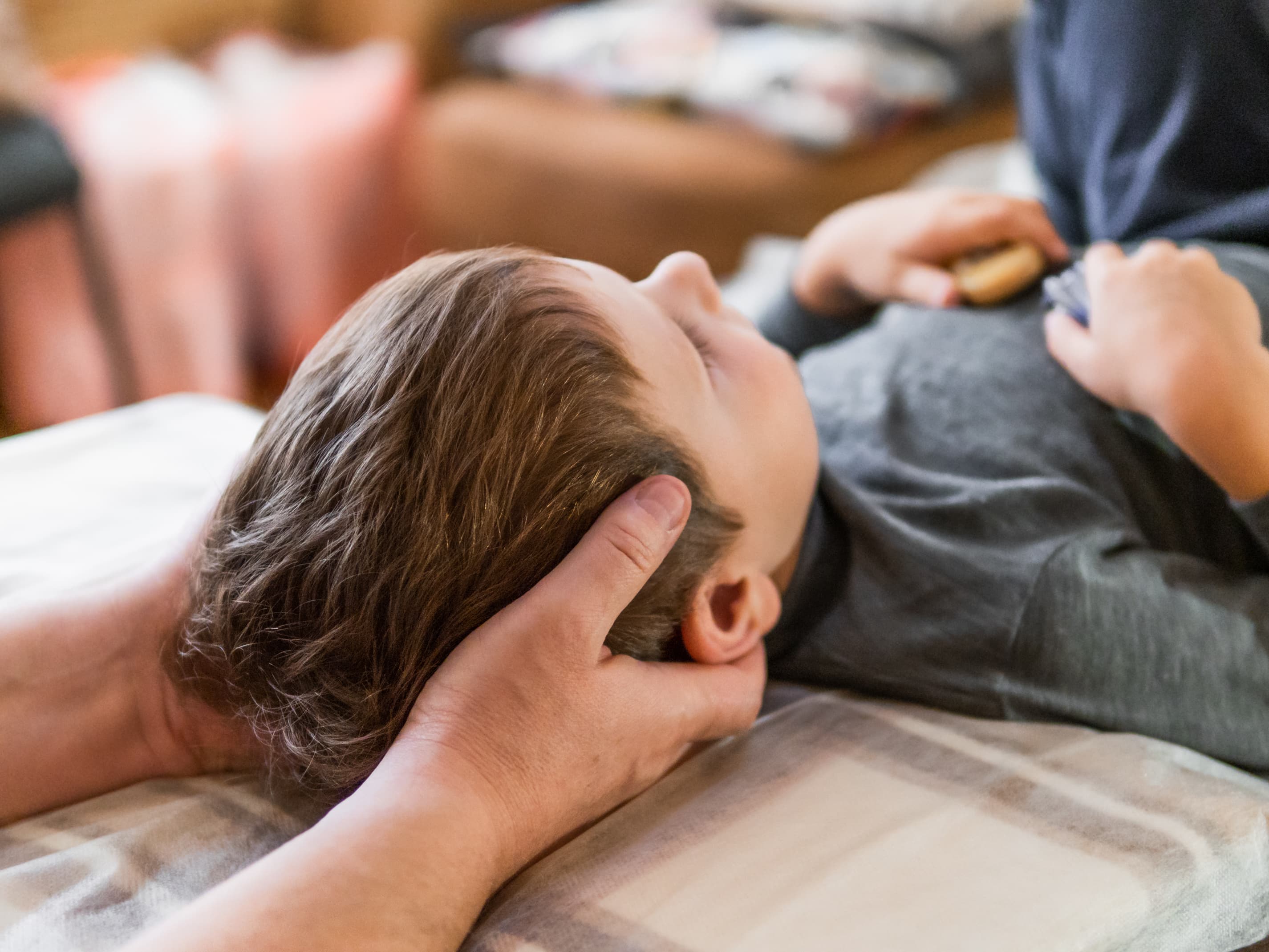 Adult hands gently cradle the head of a young child resting with eyes closed.